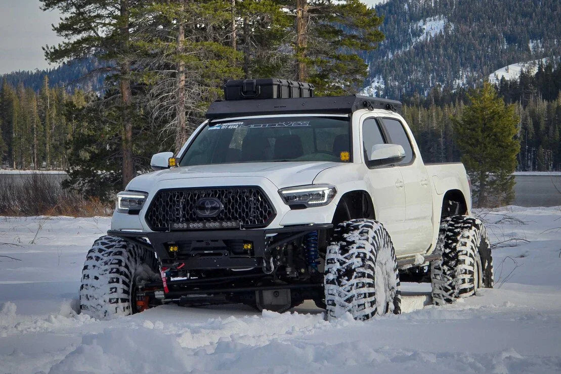 Lifted white Toyota Tacoma with off-road tires and aftermarket headlights in snowy wilderness