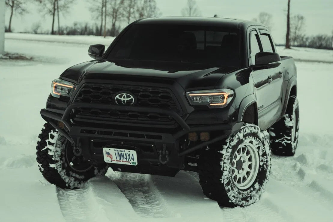 Toyota Tacoma with aftermarket Evo headlights and off-road tires on snowy terrain