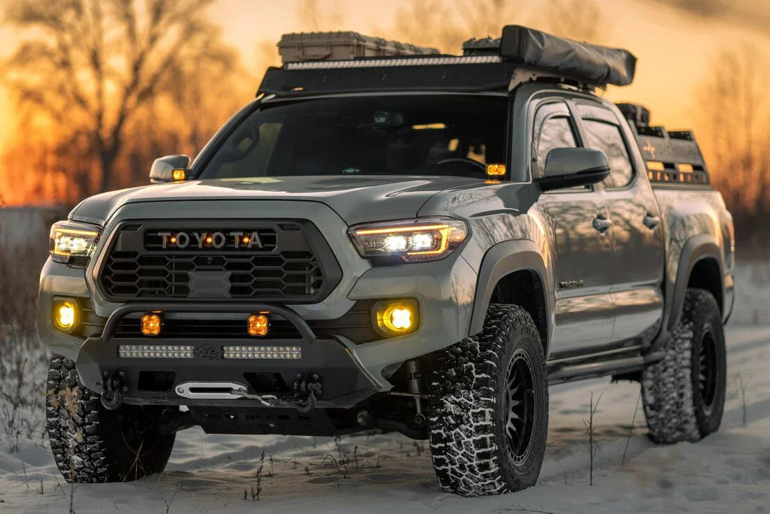 Toyota Tacoma with XB Evo headlights, overlanding gear, and off-road accessories in snow