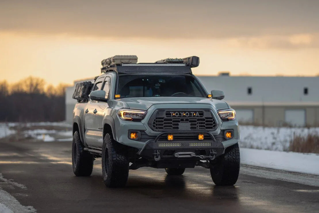 Toyota Tacoma with off-road lights, rooftop gear, and snow background at sunset