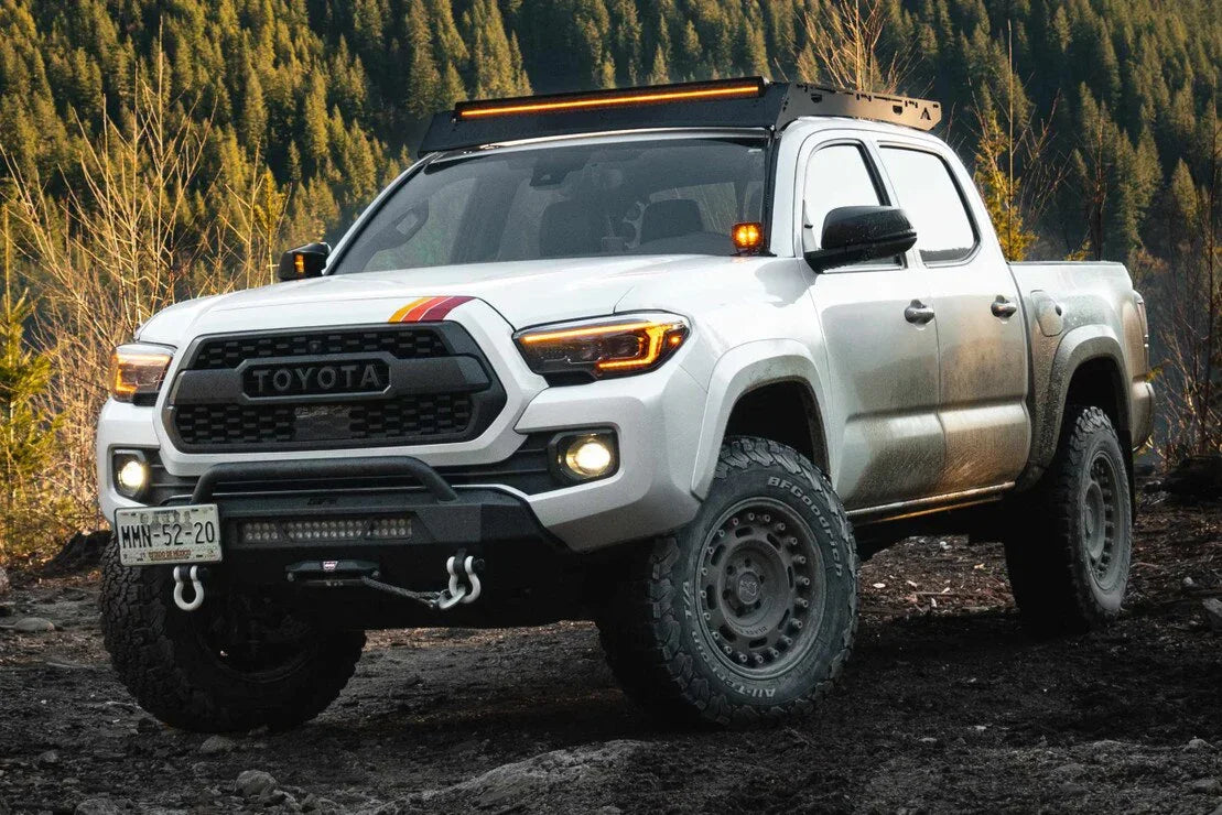 Toyota Tacoma with off-road tires, XB Evo headlights, and LED roof light in a forest setting