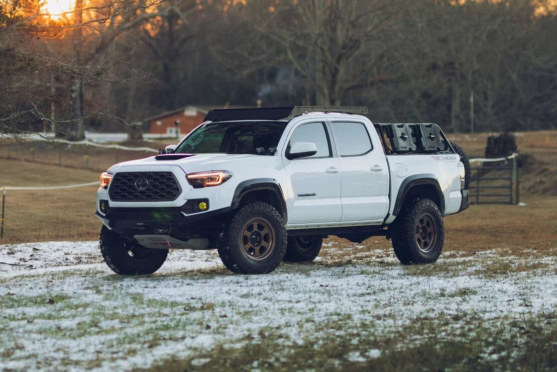 White Toyota Tacoma TRD 4x4 pickup with off-road tires and custom headlights parked outdoors