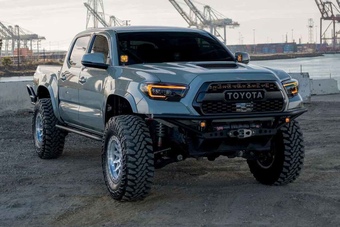 Lifted Toyota Tacoma with XB Evo headlights and off-road tires parked by waterfront cranes