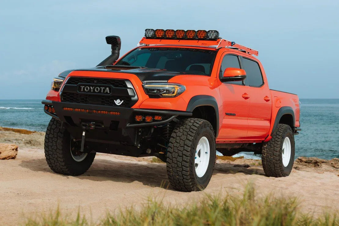Lifted orange Toyota Tacoma with off-road accessories and LED headlights on a beach