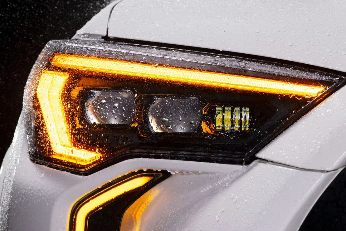 Close-up of a wet LED headlight on a white Toyota Tacoma with amber DRL accent lighting.