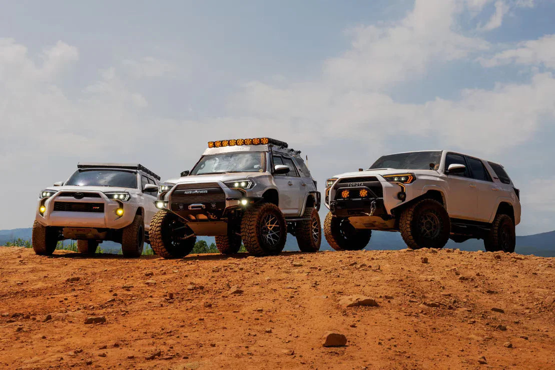 Three white Toyota 4Runner SUVs with off-road accessories on a dirt trail under blue sky