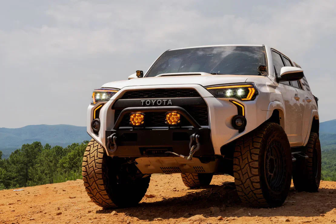 White Toyota 4Runner with off-road accessories and rugged tires on a dirt trail in the mountains