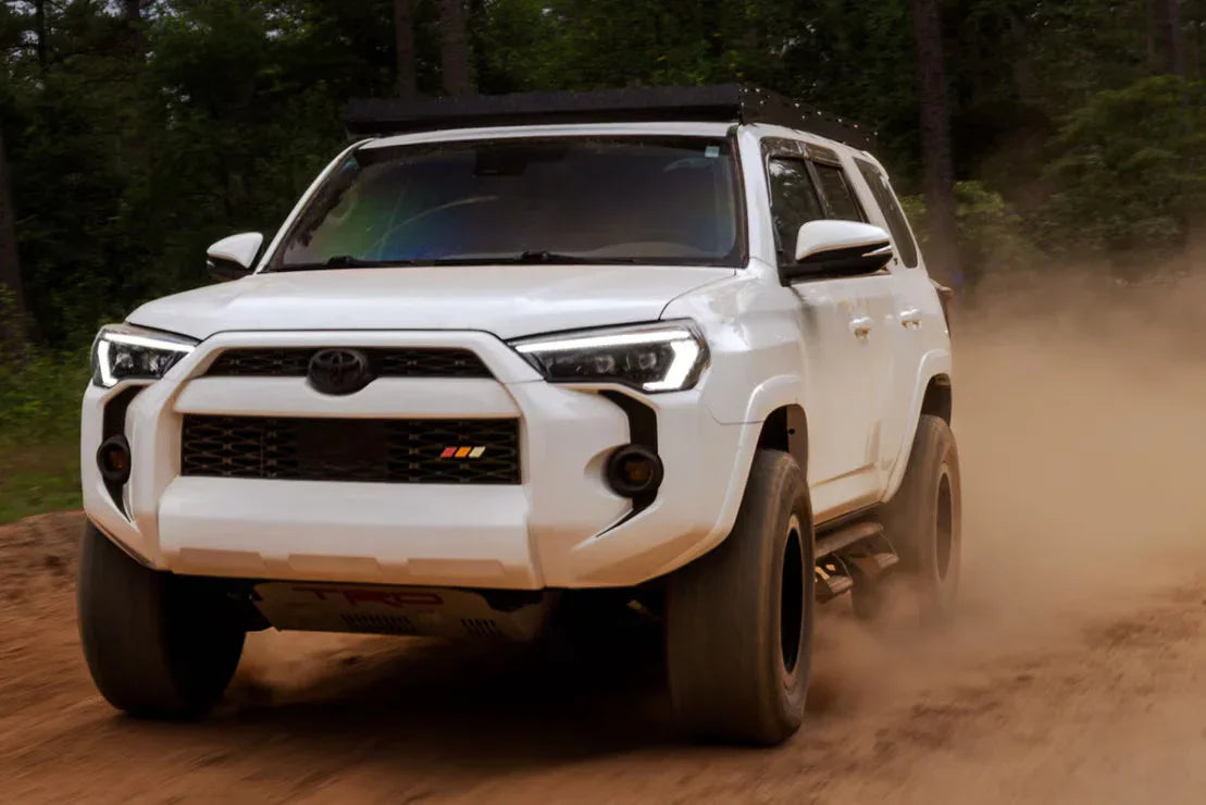 White Toyota 4Runner off-road SUV kicking up dust on a dirt trail in the forest