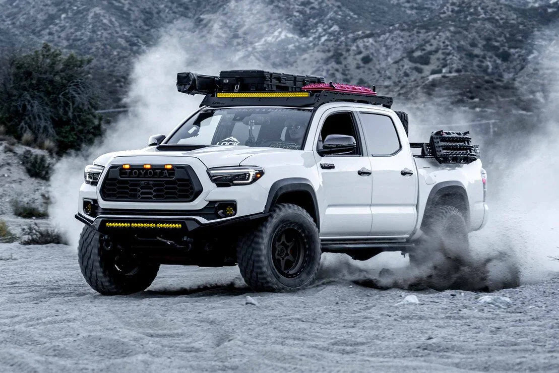 Lifted white Toyota Tacoma with off-road gear and Evo Hybrid headlights driving on dirt trail