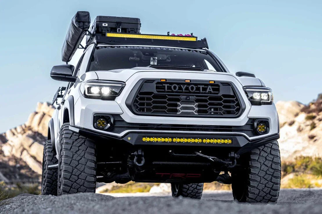 Front view of a white Toyota Tacoma with off-road accessories and LED headlights on a rocky trail