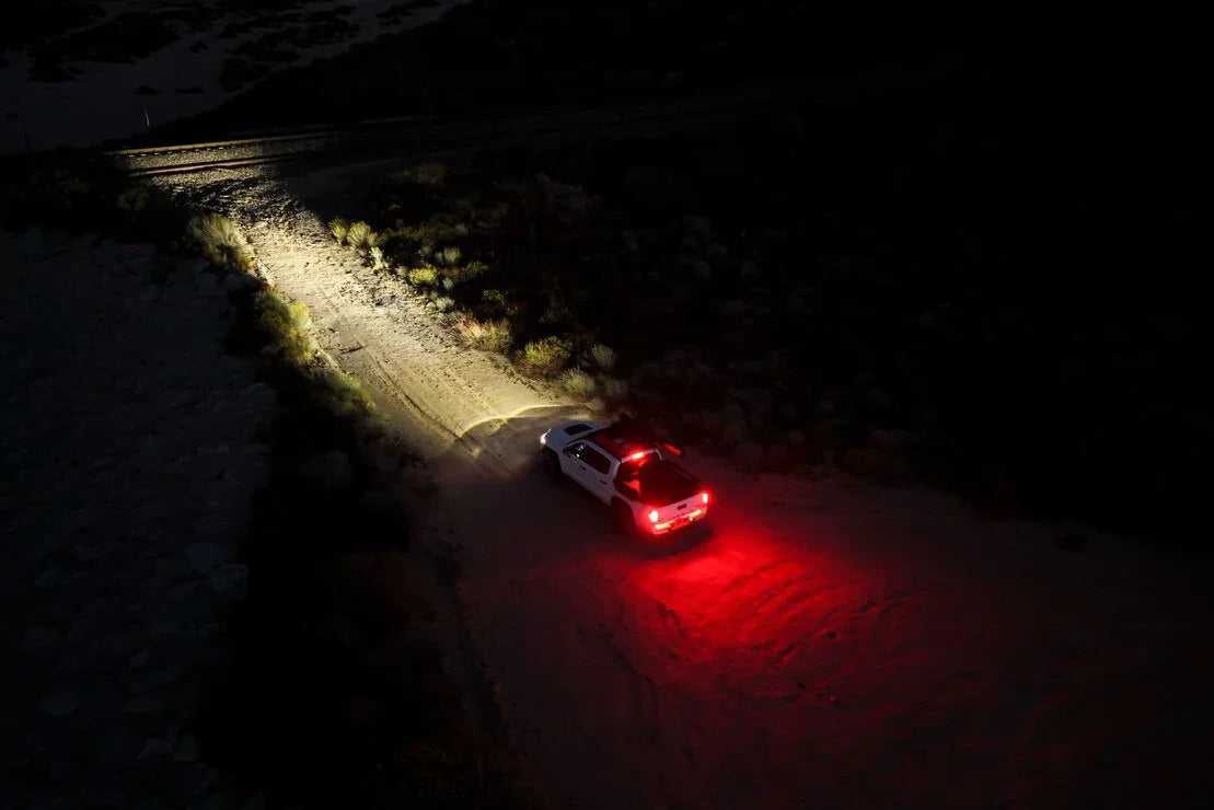 Toyota Tacoma off-road at night with bright LED headlights and red taillights illuminating trail