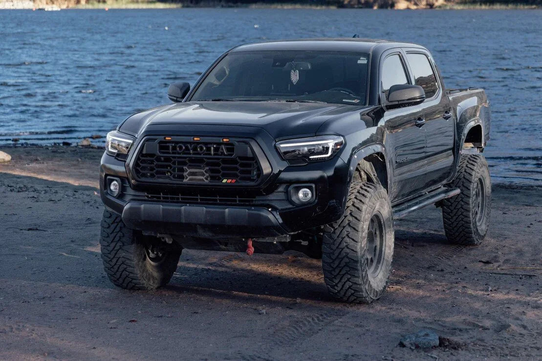 Lifted black Toyota Tacoma with XB Evo Hybrid headlights on a lakeside dirt path