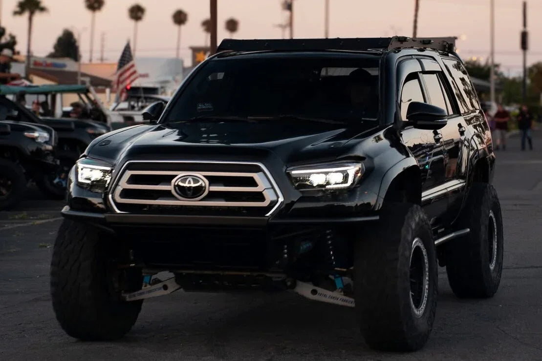 Lifted Toyota Tacoma with aftermarket XB Evo Hybrid headlights on city street at dusk