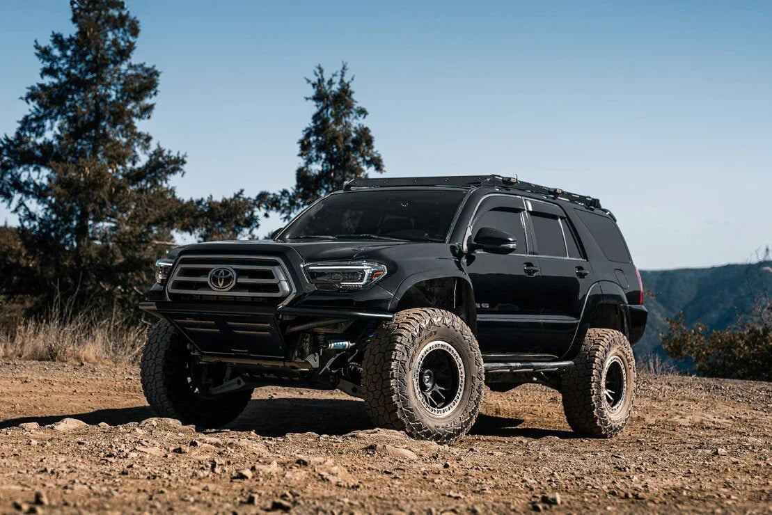 Lifted black Toyota Tacoma SUV with off-road tires and hybrid headlights on a rugged dirt trail