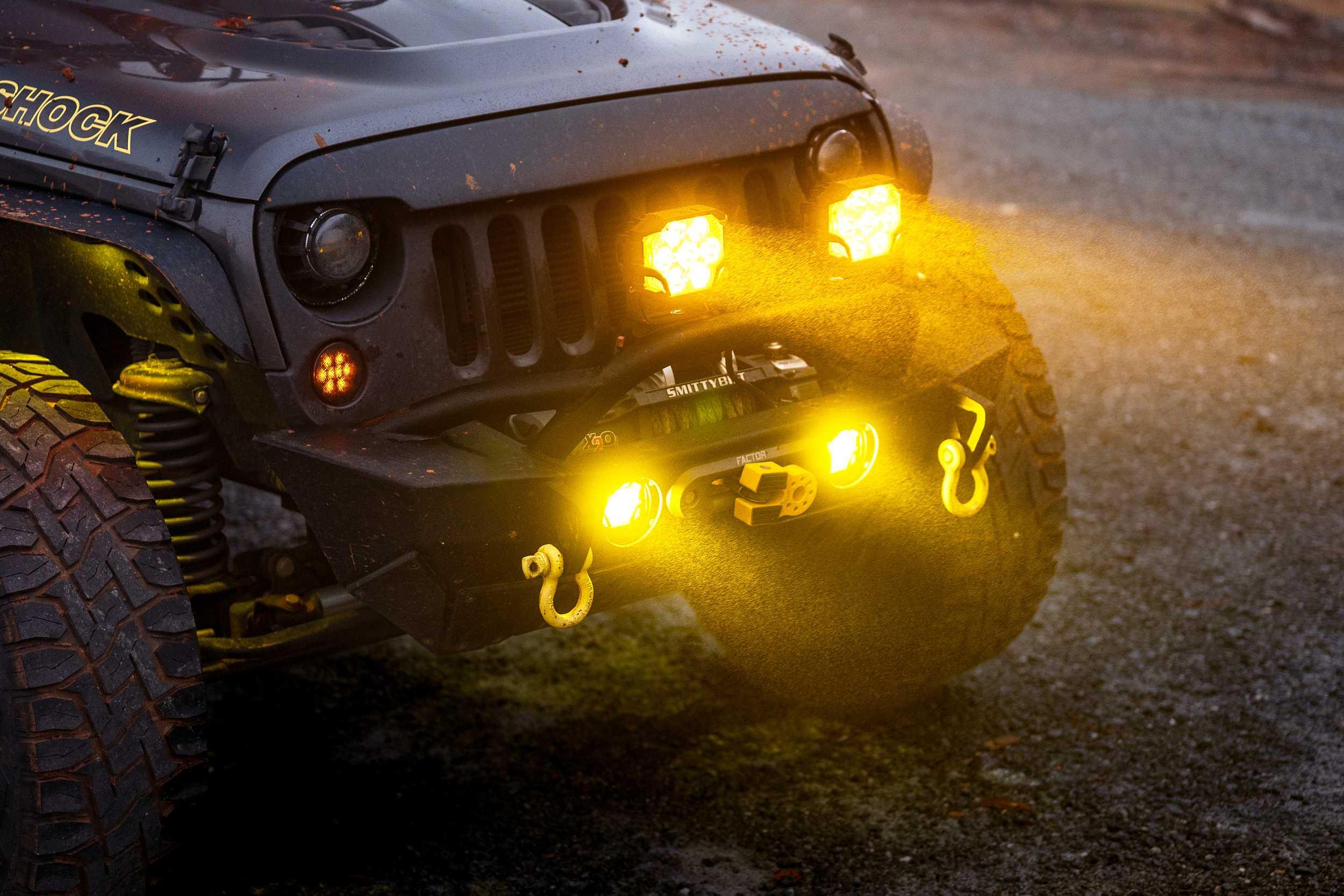 Off-road vehicle front with yellow LED lights, tow hooks, and rugged tires on dirt