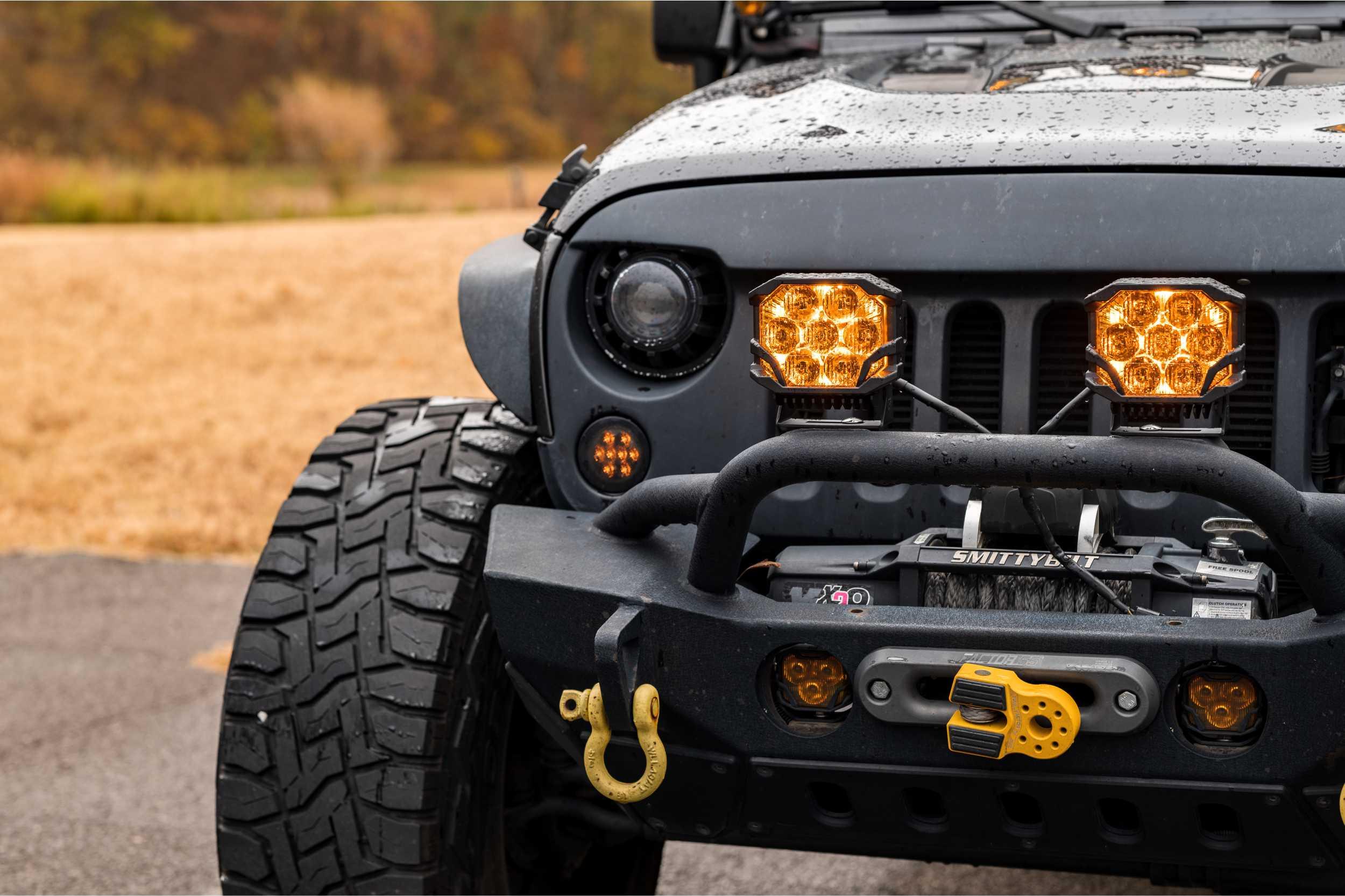 Close-up of Jeep Wrangler with off-road bumper, winch, amber LED lights, and wet tire