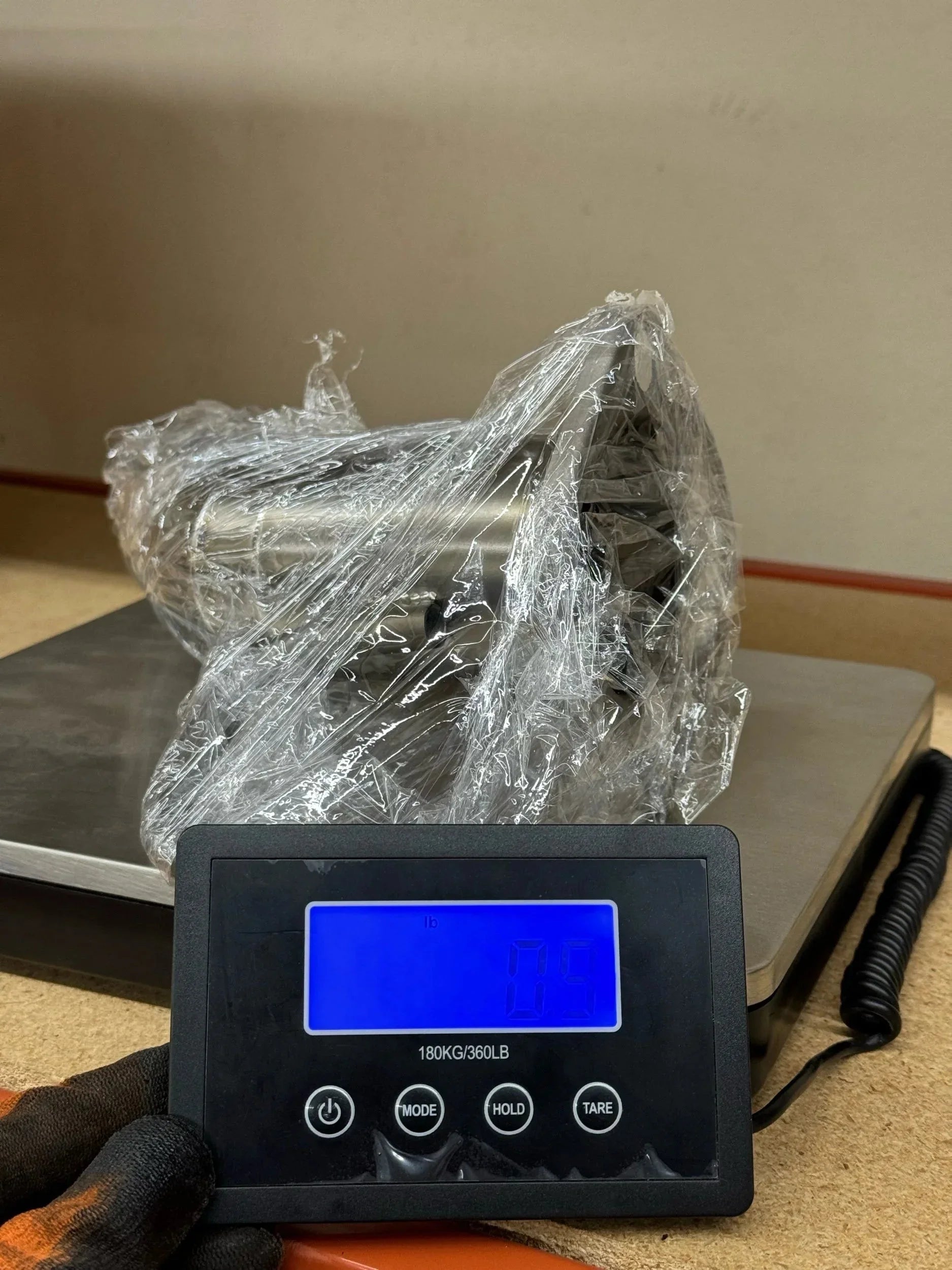 Metal vehicle accessory wrapped in plastic on digital scale, overlanding gear component