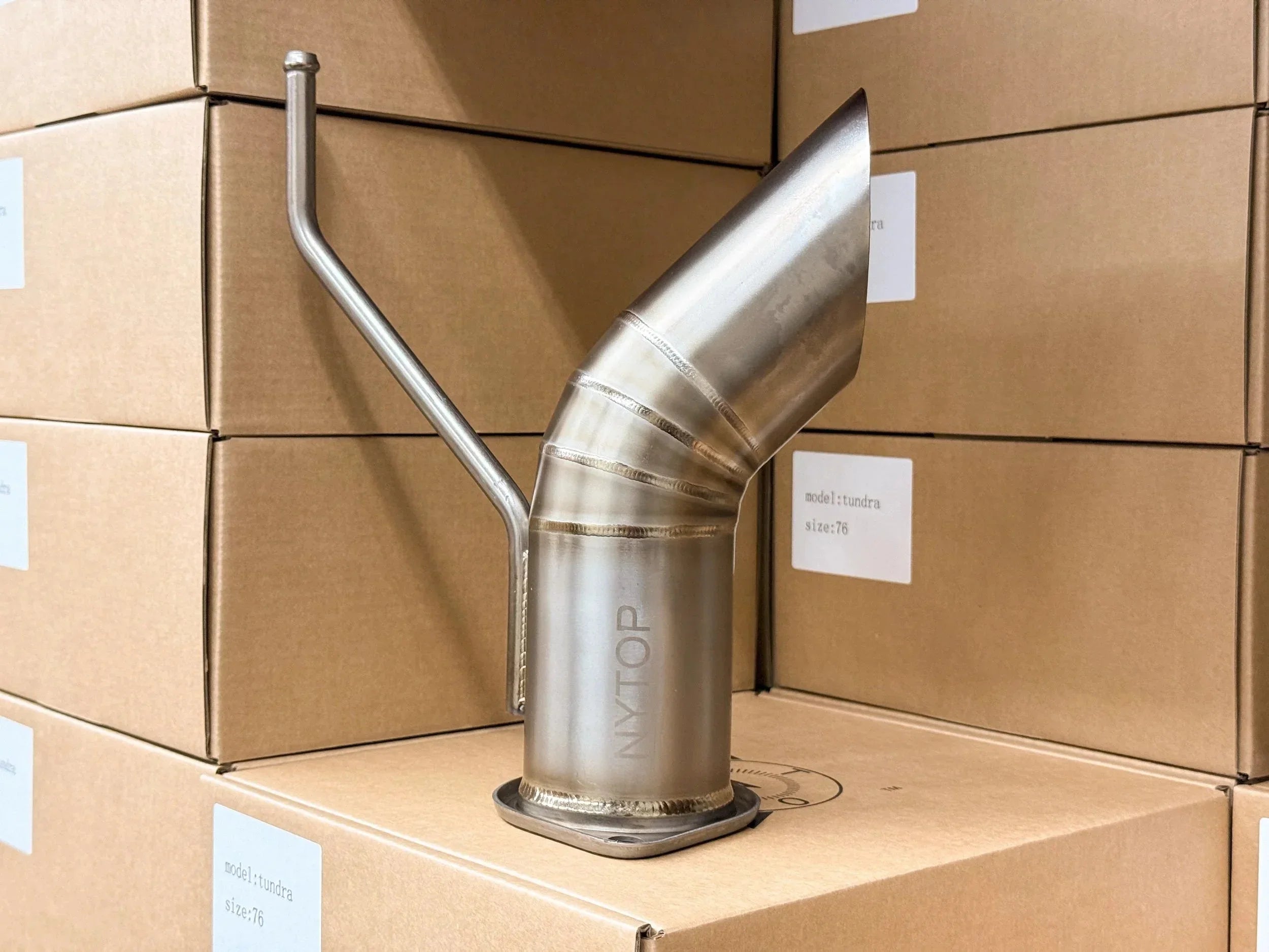 Stainless steel exhaust tip for Toyota Tundra, angled cut, on stacked cardboard boxes