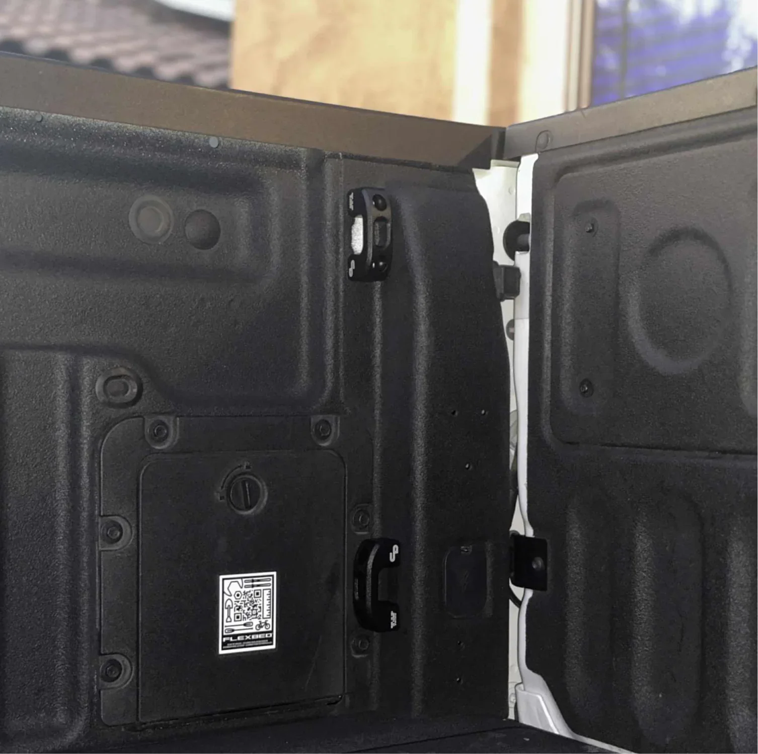 Close-up of truck bed corner with black tie-downs, textured liner, and access panel, ideal for overlanding gear.