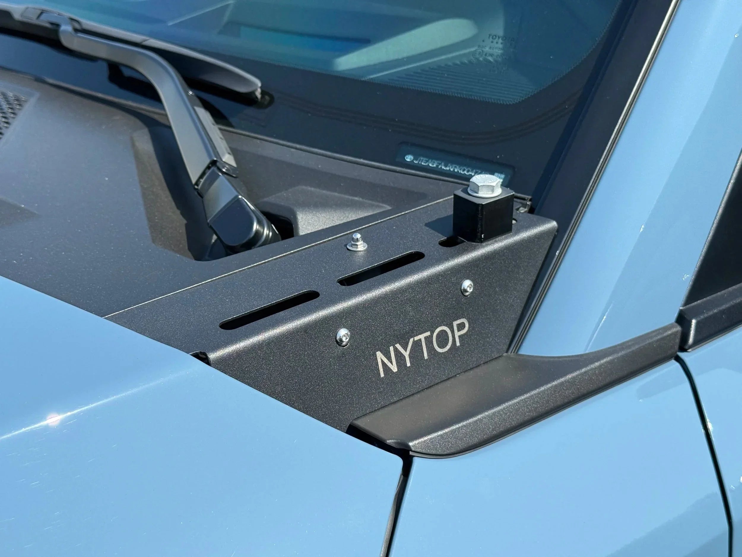 Overland accessory hood mount bracket installed on Toyota vehicle cowl, labeled NYTOP.