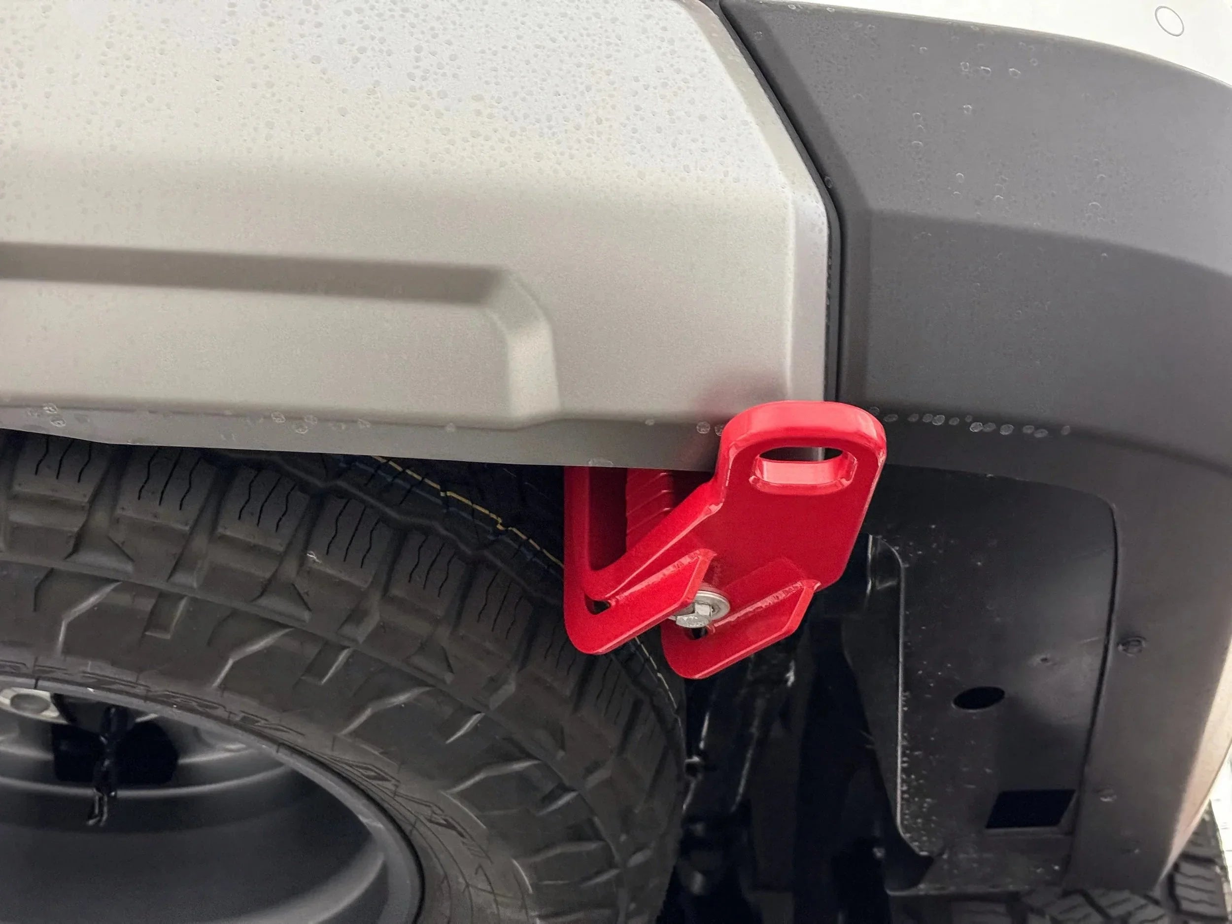 Red rear recovery point attached to off-road vehicle bumper above rugged tire