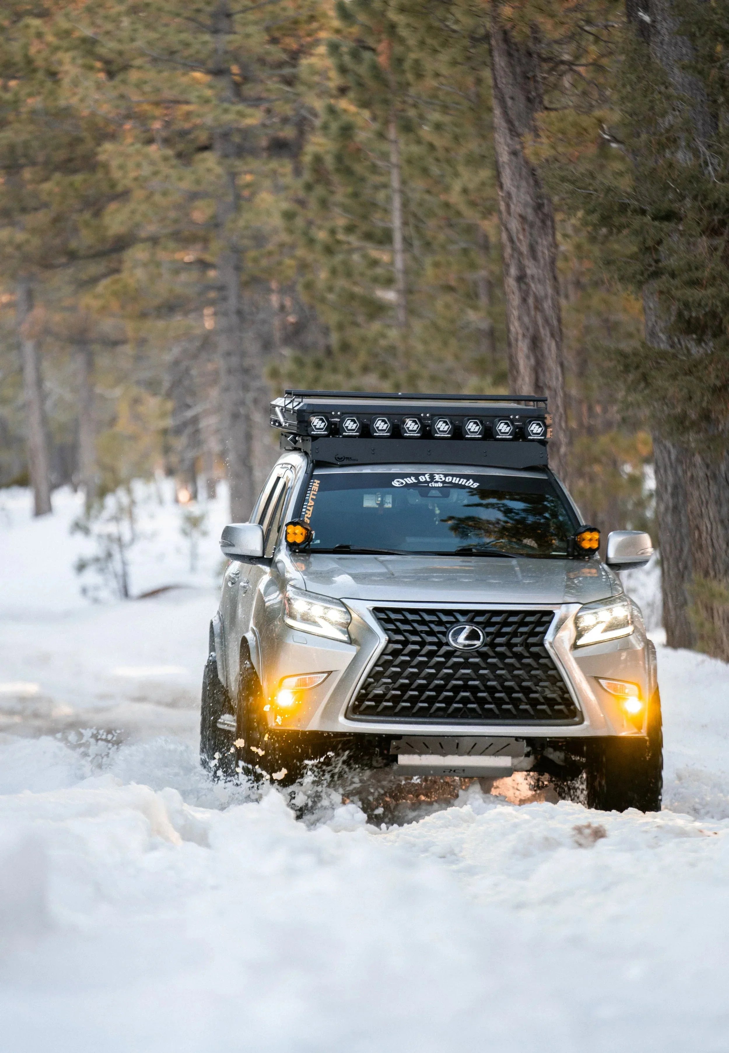 Overland-ready Lexus SUV with roof rack and LED lights driving through snowy forest trail