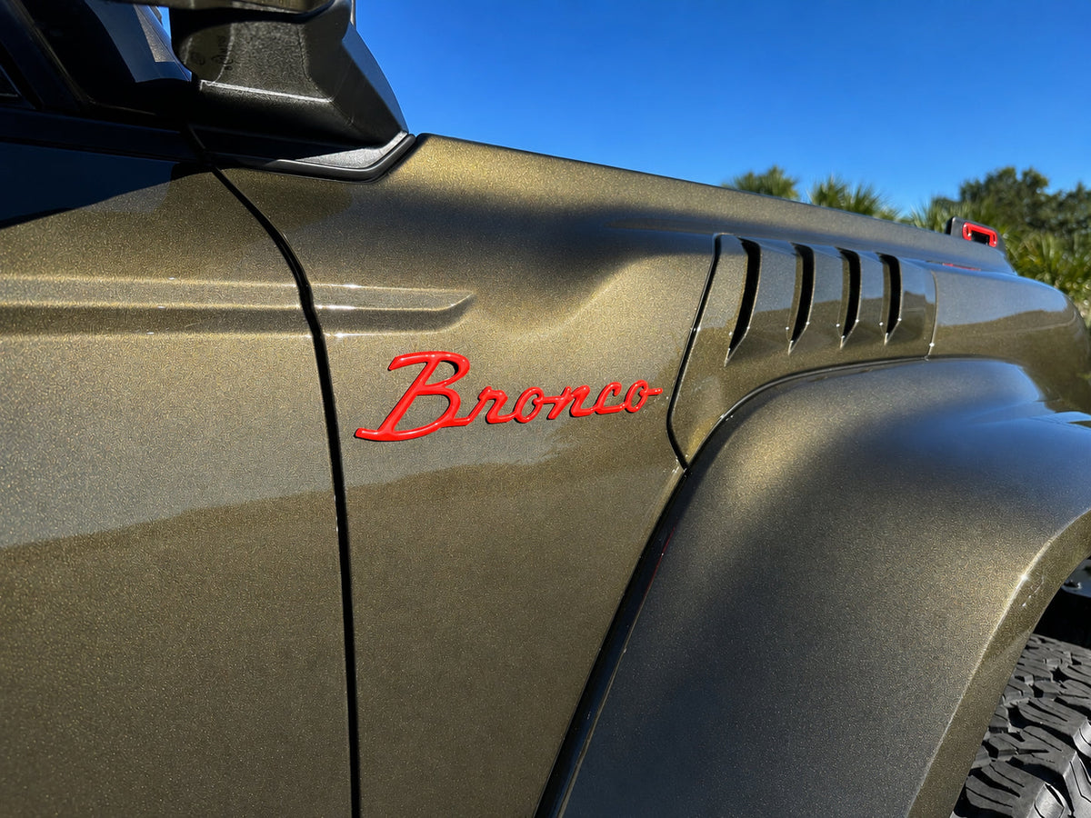 Tufskinz red Bronco script badge on the front fender of an olive green Ford Bronco, beside the fender vents