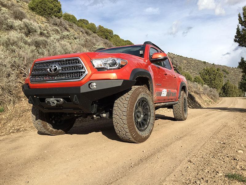 Toyota Tacoma with off-road front bumper driving on a dirt trail in rugged terrain