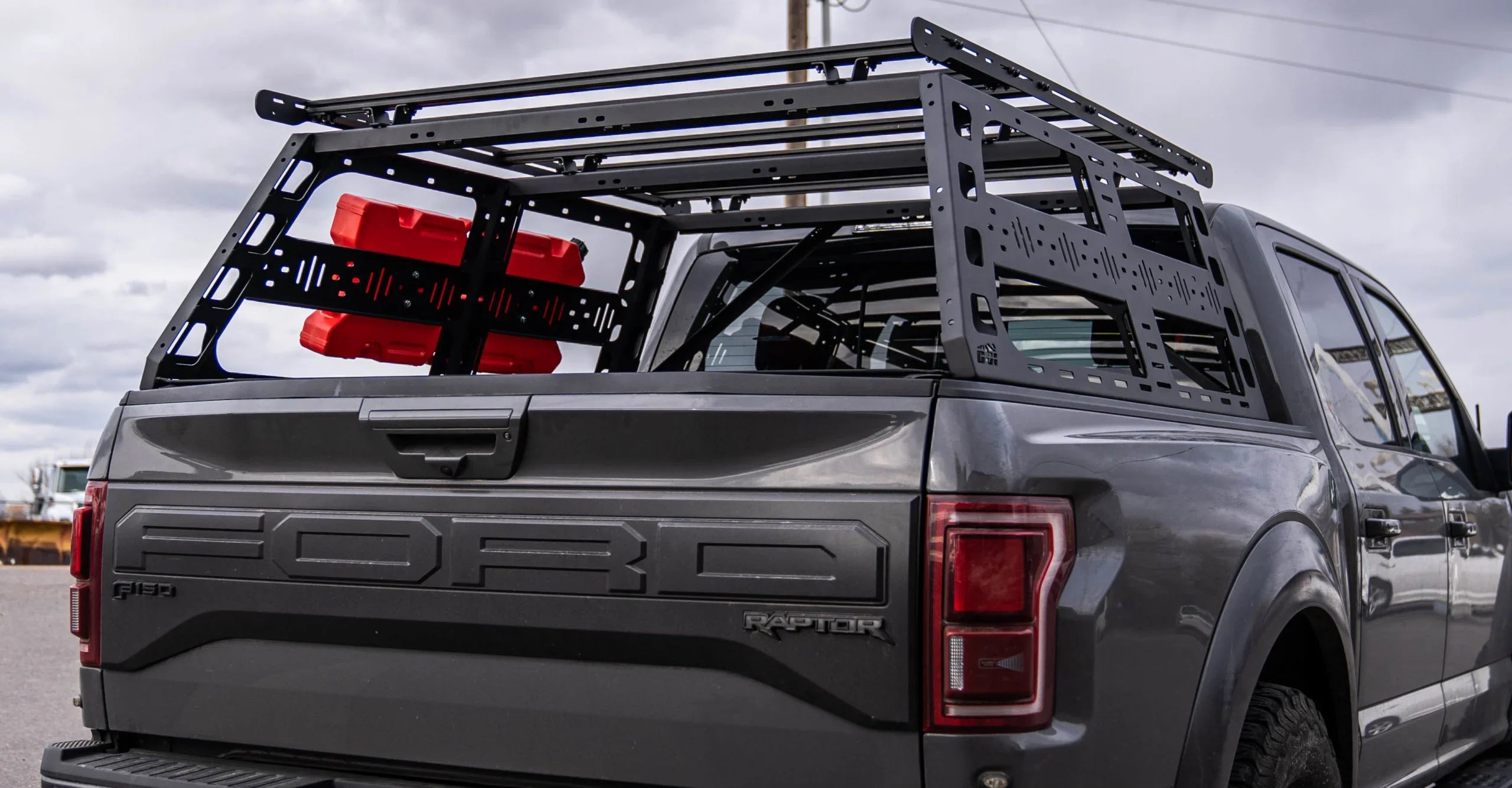 Off-road bed rack with red fuel containers mounted on a Ford Raptor F-150 pickup truck