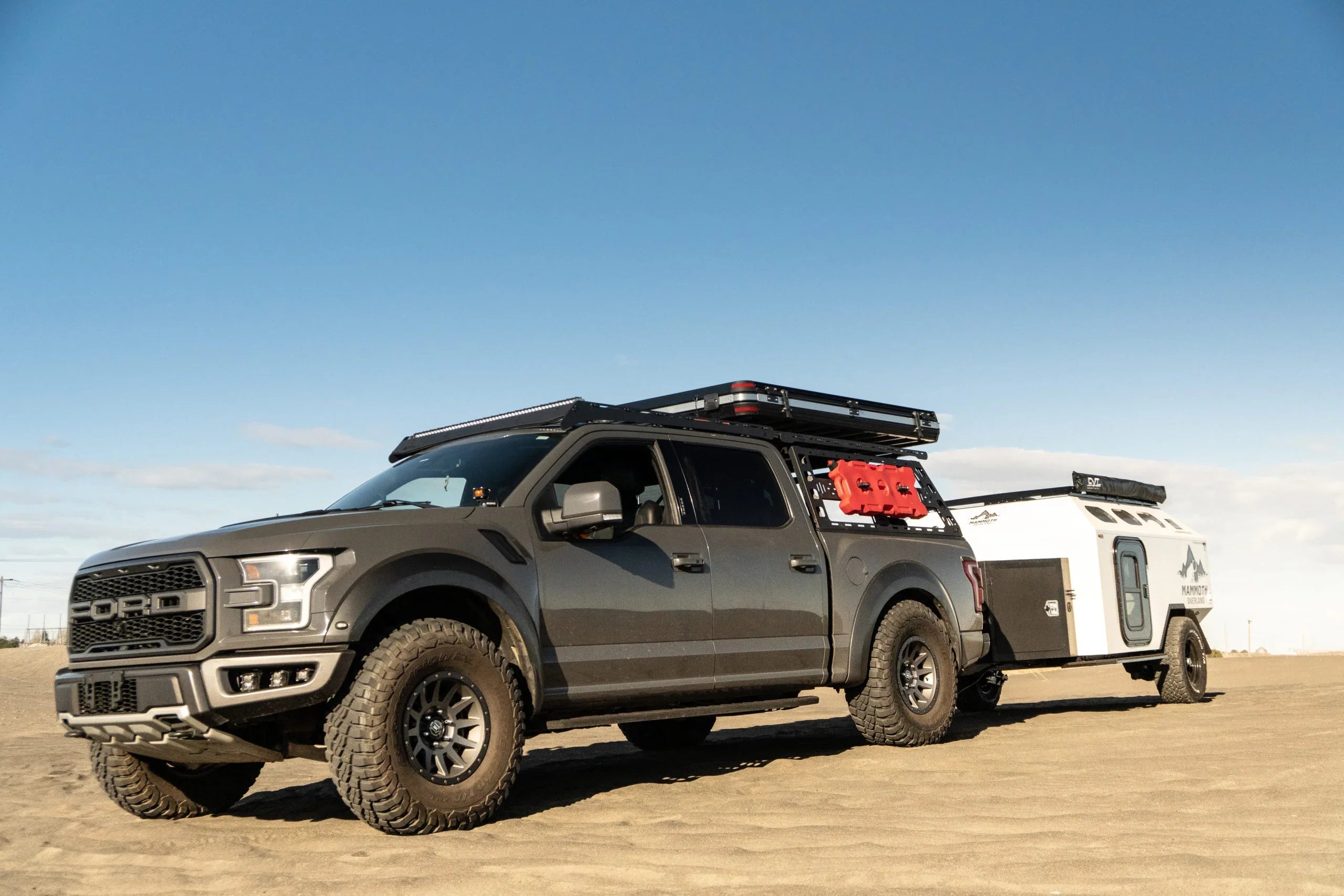Ford Raptor with off-road bedrack and camping trailer on desert sand, overlanding setup