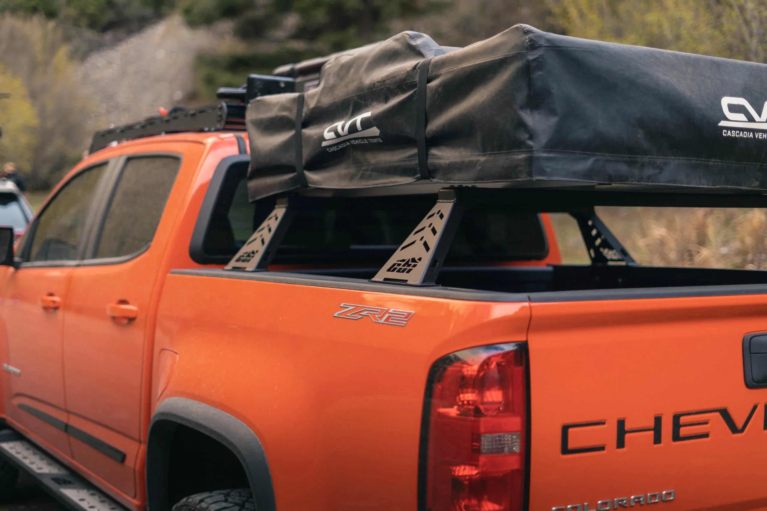 Orange Chevy Colorado with overland bed bars and rooftop tent in outdoor setting