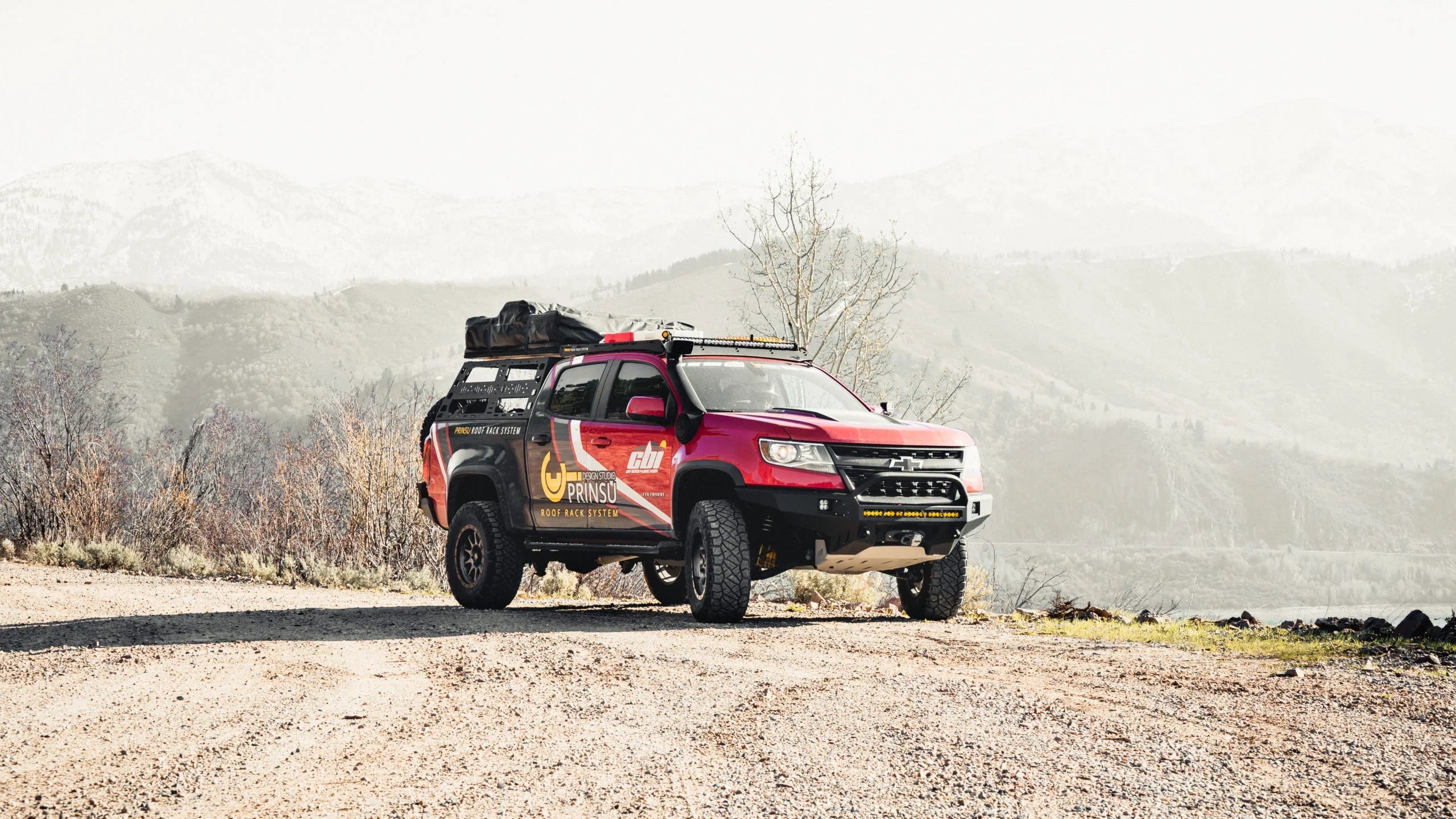 Chevy Colorado off-road truck with bed rack and rooftop gear on rugged dirt trail