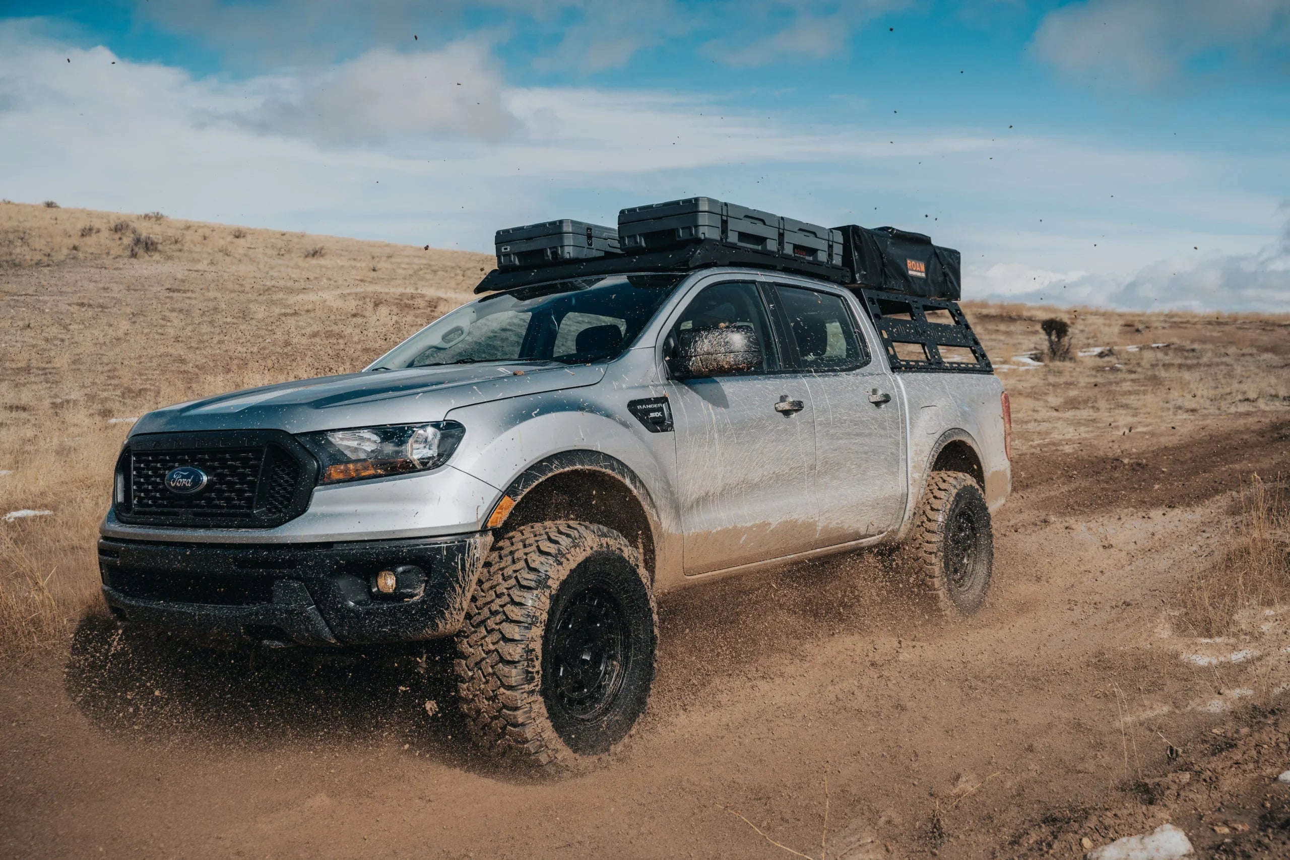 Ford Ranger with off-road bed rack and gear, driving on rugged trail