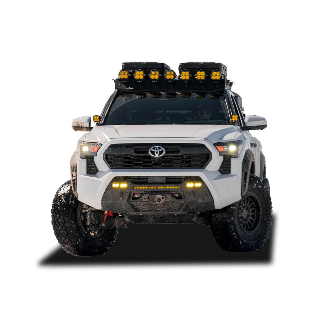 Front view of a white 2024 Toyota Tacoma with off-road bumper, rooftop lights, and rugged tires