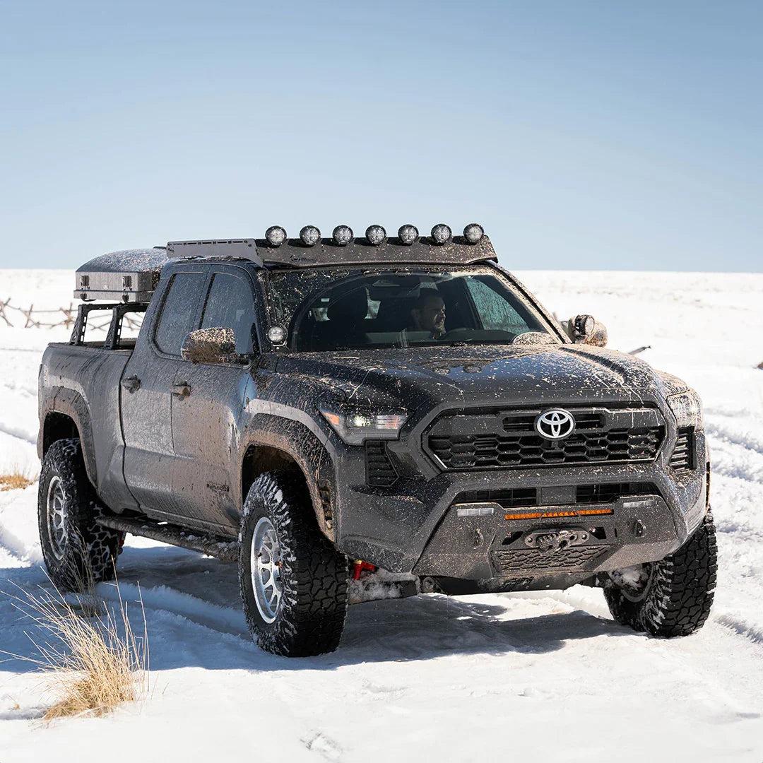 Toyota Tacoma off-road truck with roof lights and mud splatter driving in snowy terrain