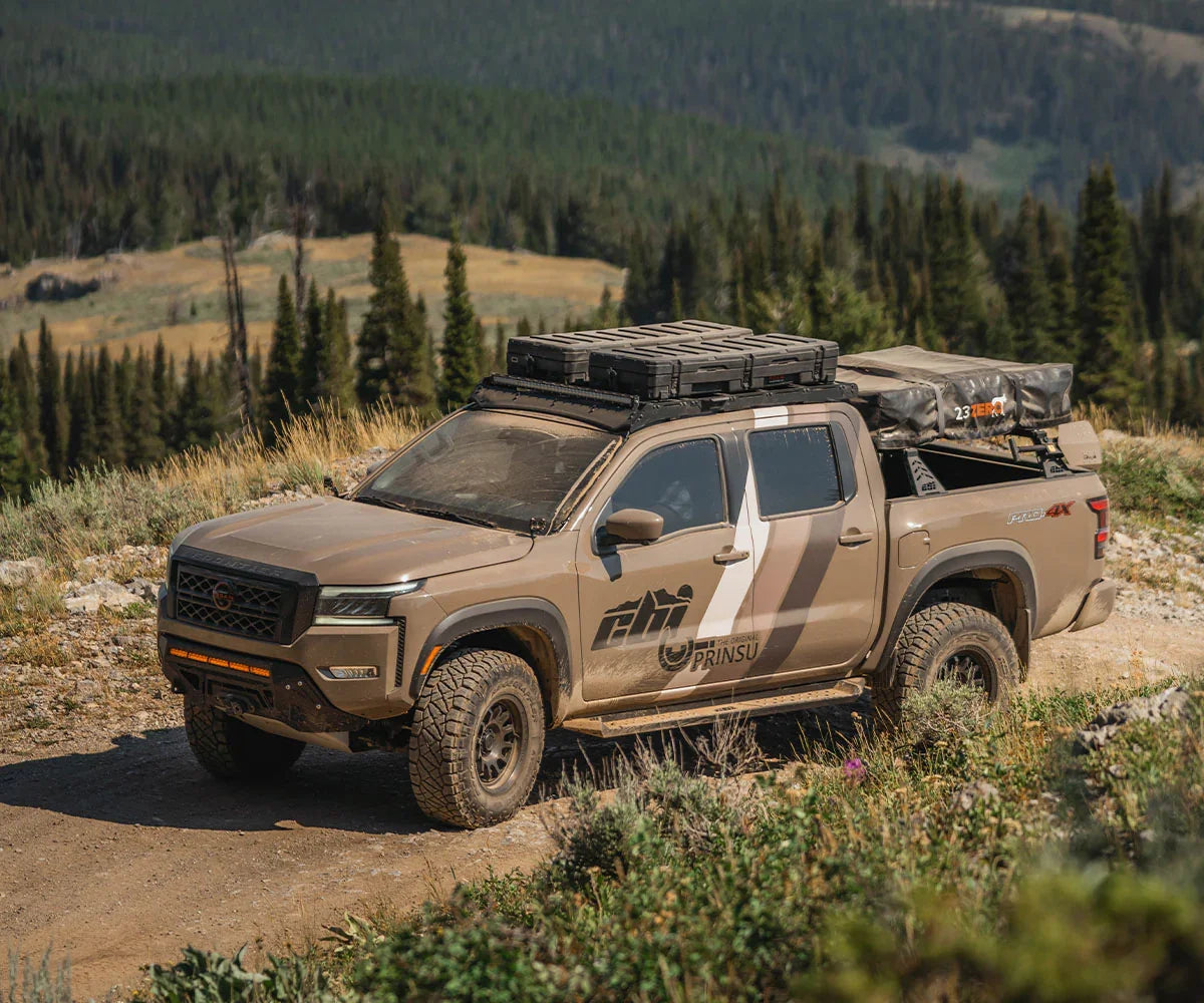 Nissan Frontier with off-road bumper, roof rack, and camping gear on rugged mountain trail