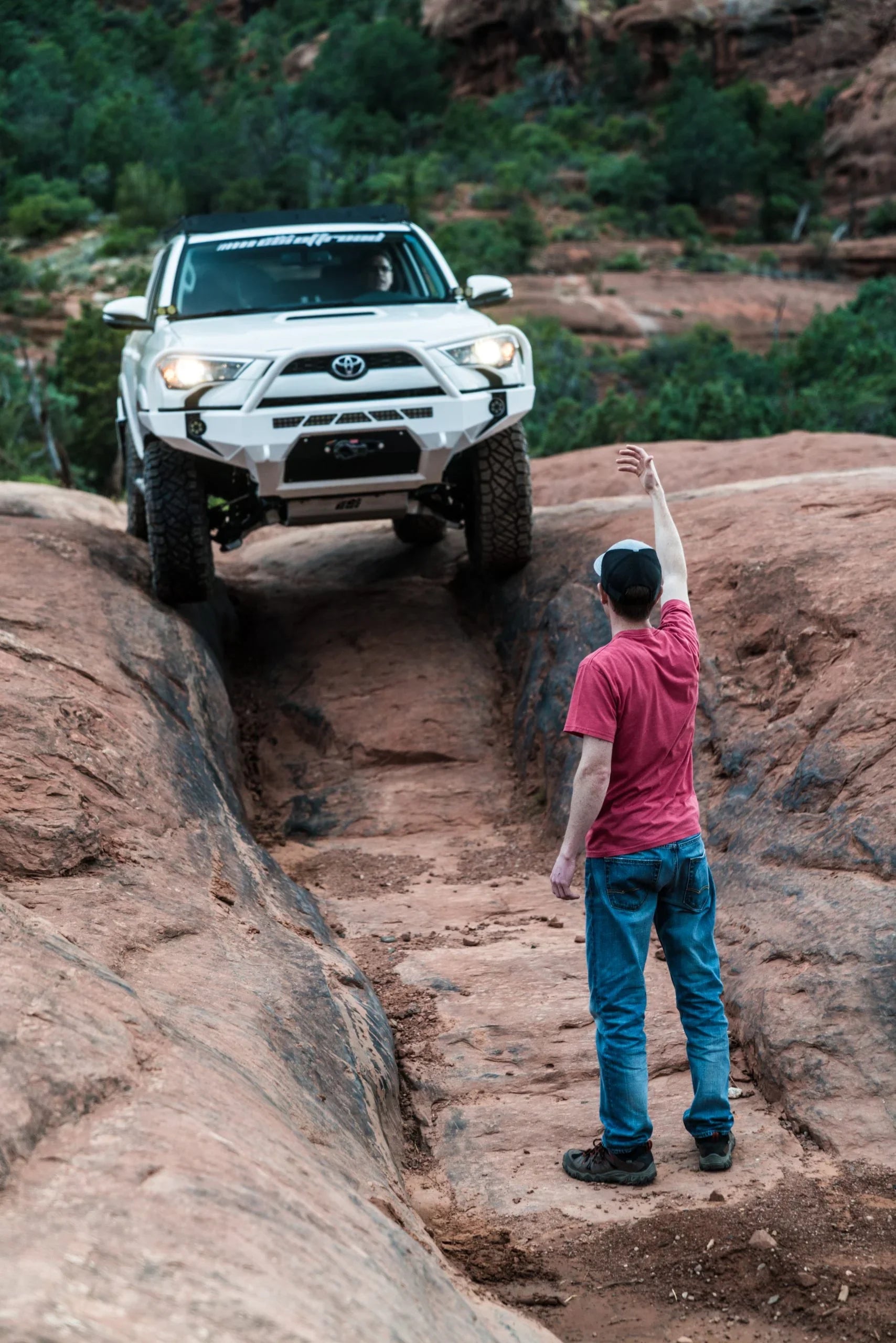 Toyota 4Runner with adventure front bumper off-roading on rocky terrain, guided by a man.