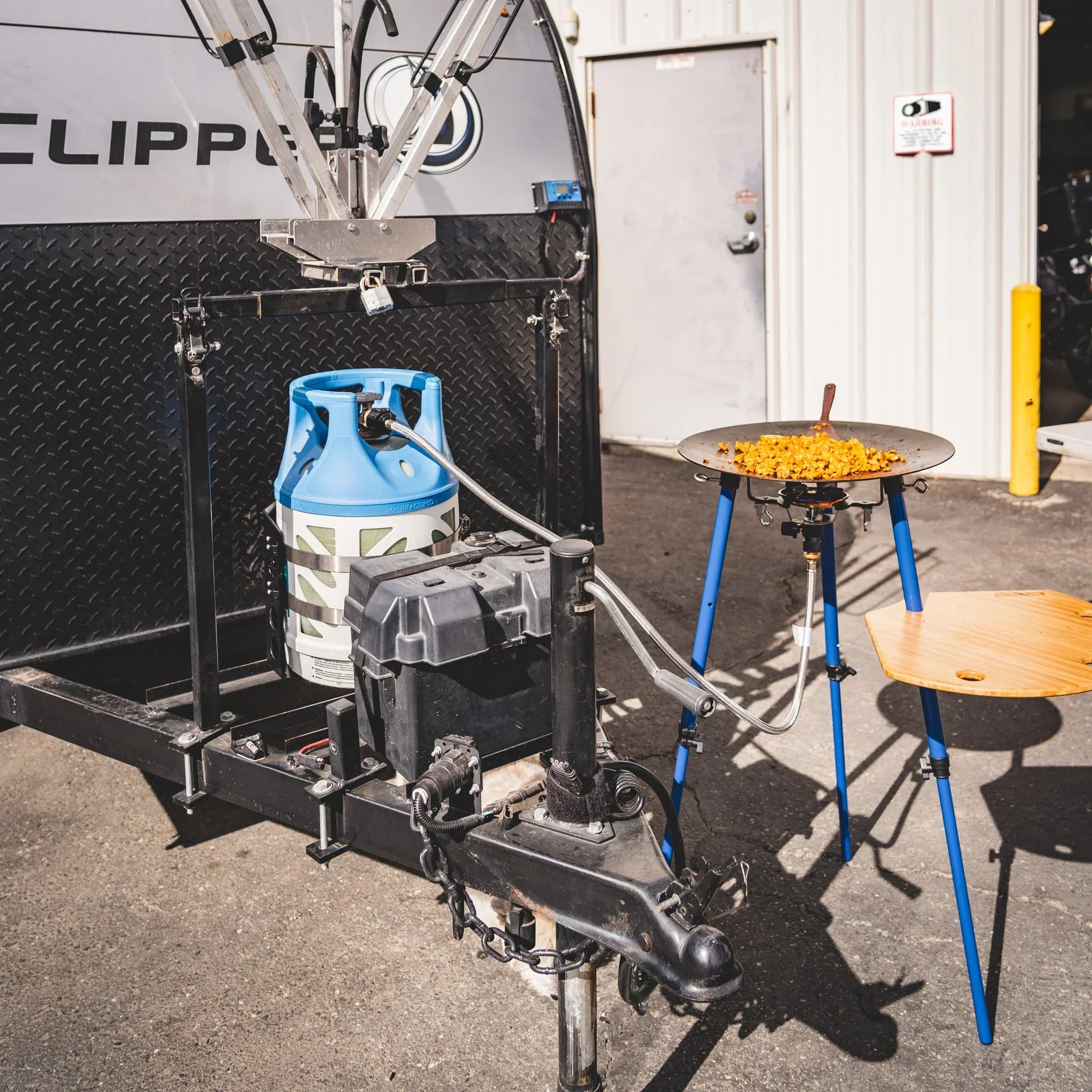 Portable propane camp stove setup with griddle cooking food, attached to trailer hitch outdoors