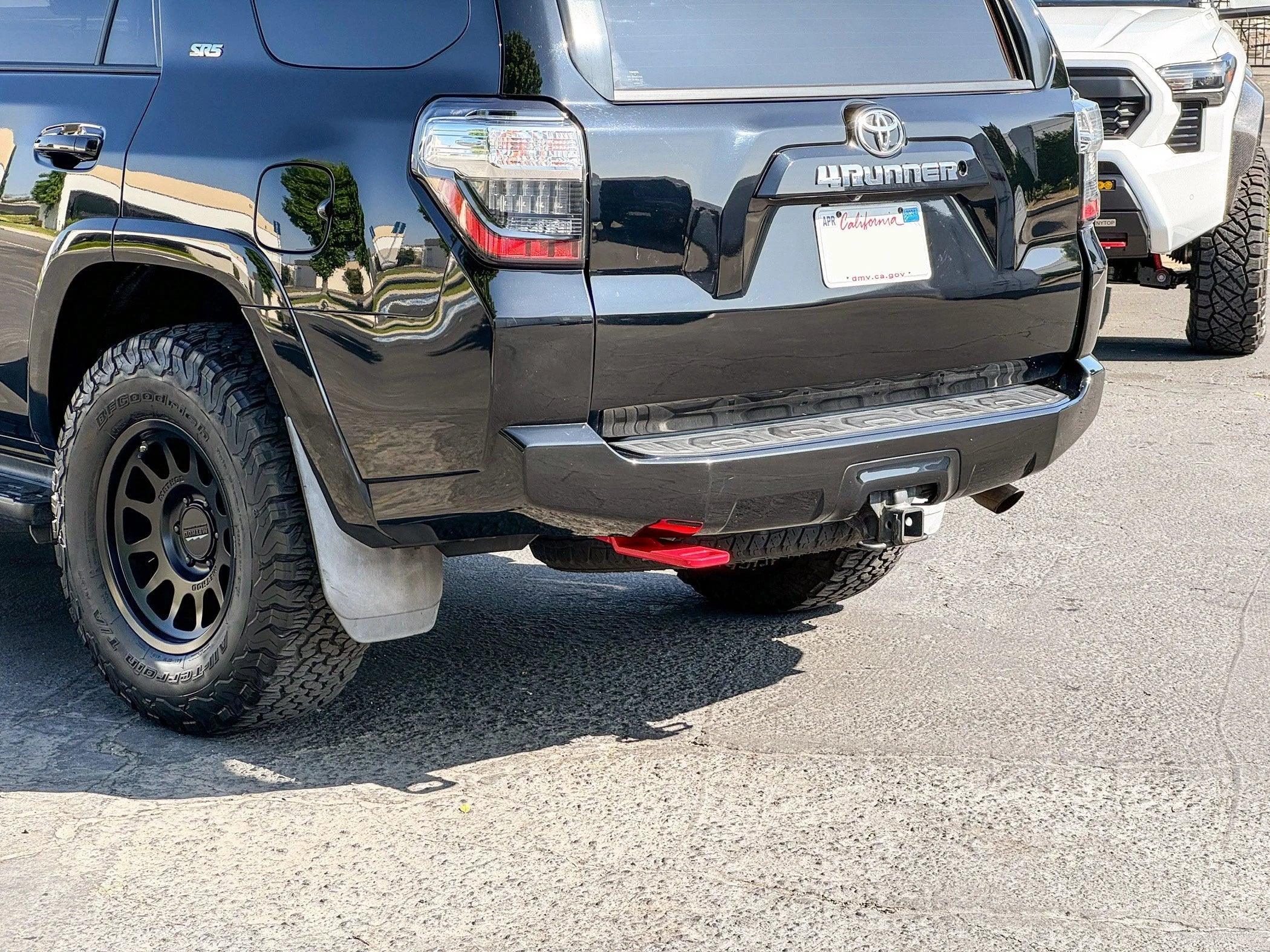 Rear view of a black Toyota 4Runner with off-road tires, trailer hitch, and red recovery point