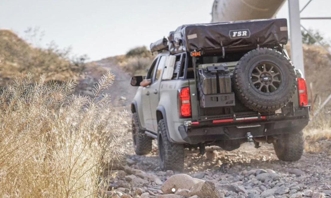 Off-road vehicle with rooftop tent and gear driving on rocky trail in desert terrain