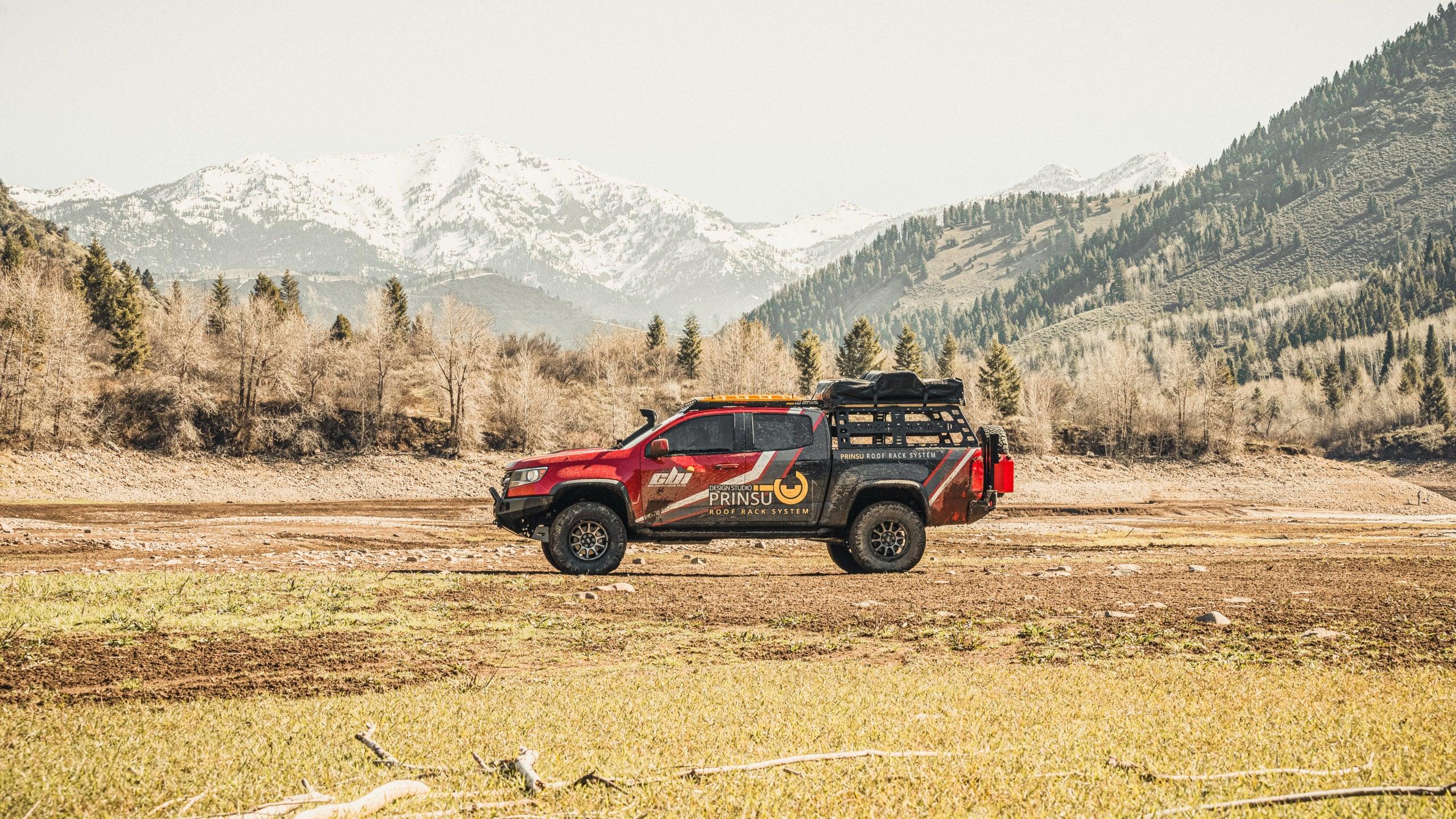 Red Chevy Colorado ZR2 off-road truck with roof rack and camping gear in mountain landscape