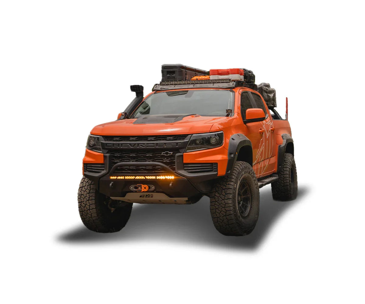 Orange Chevrolet Colorado overland truck with roof rack, off-road tires, and camping gear