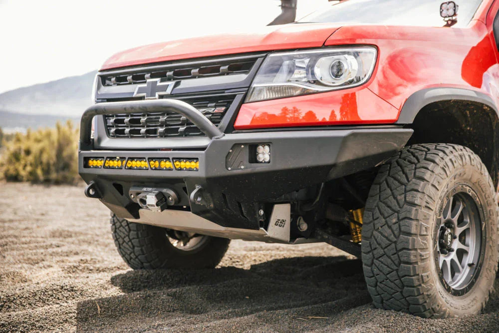 Red Chevrolet Colorado with off-road bumper, LED light bar, and rugged all-terrain tires on dirt
