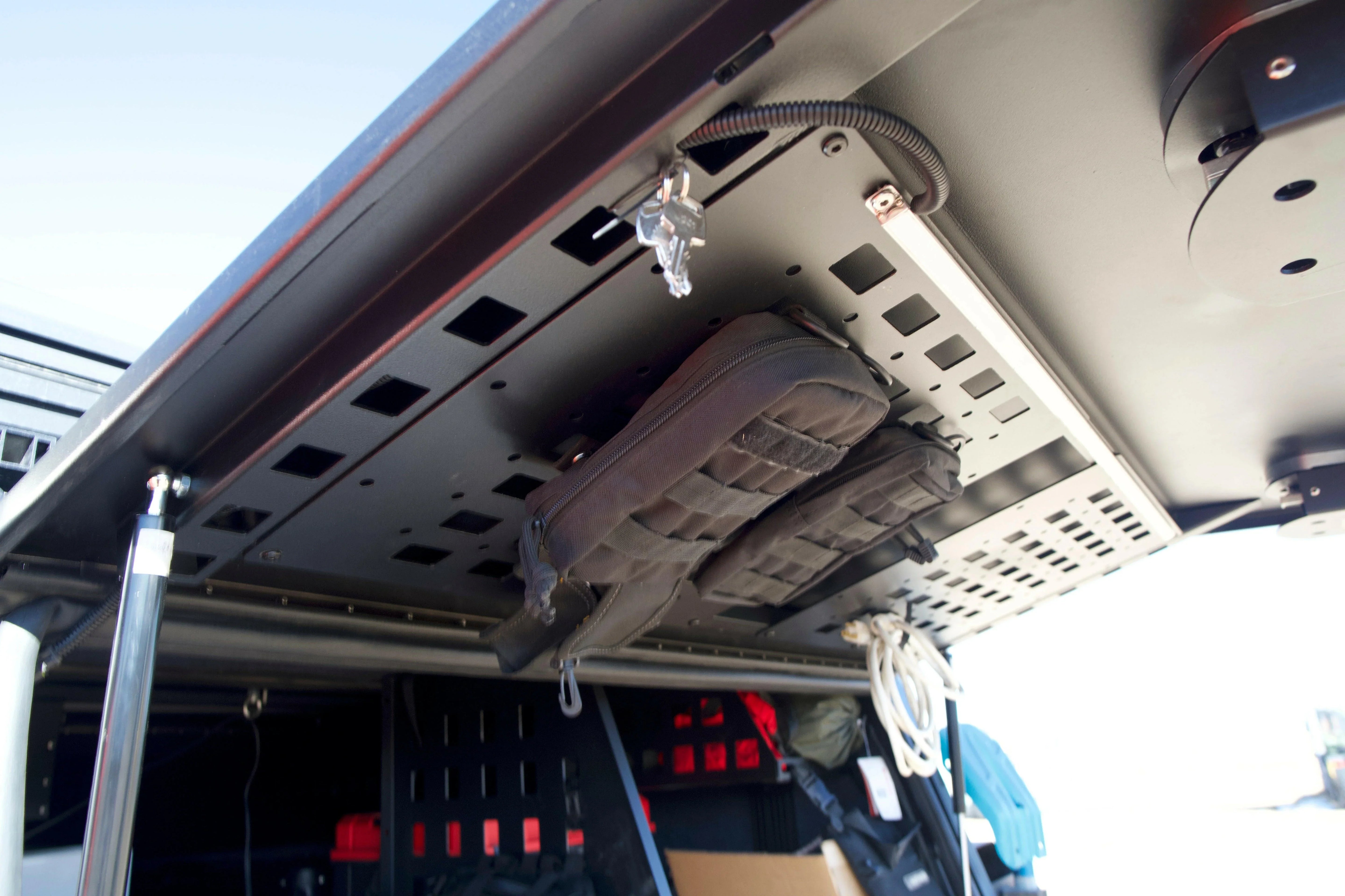Overlanding vehicle modular storage panel with secured pouches and gear, perfect for camping.