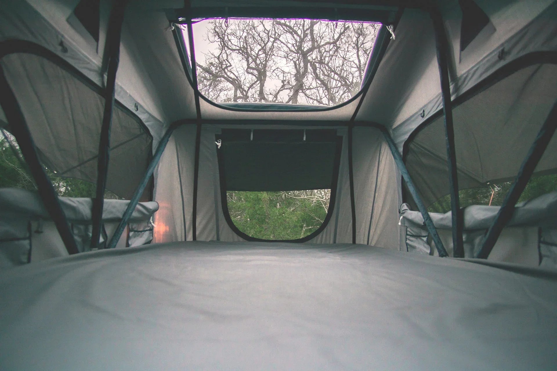 Interior view of rooftop tent for overlanding, with windows and skylight, forest outside