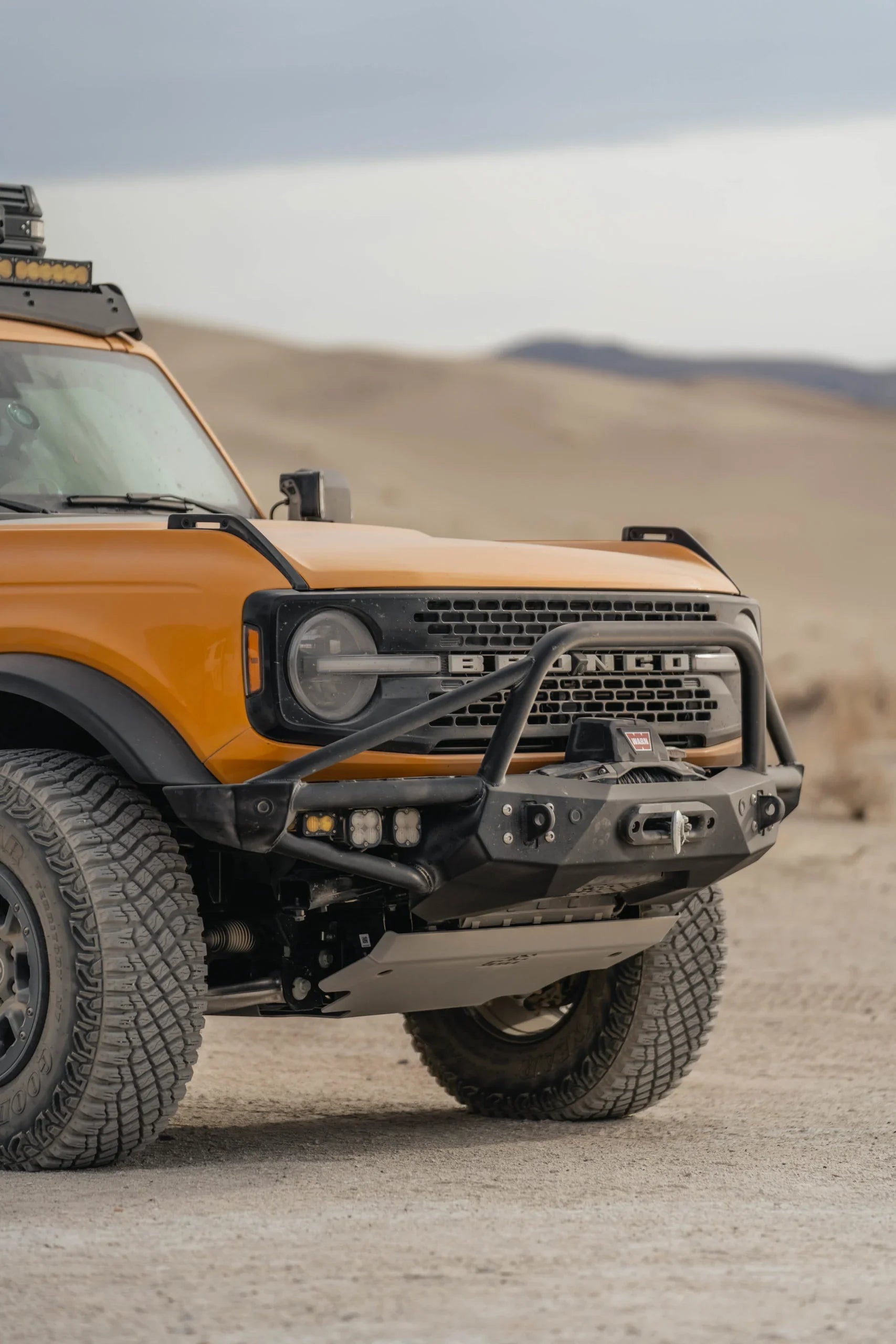 Orange Ford Bronco with off-road bumper and accessories on desert trail