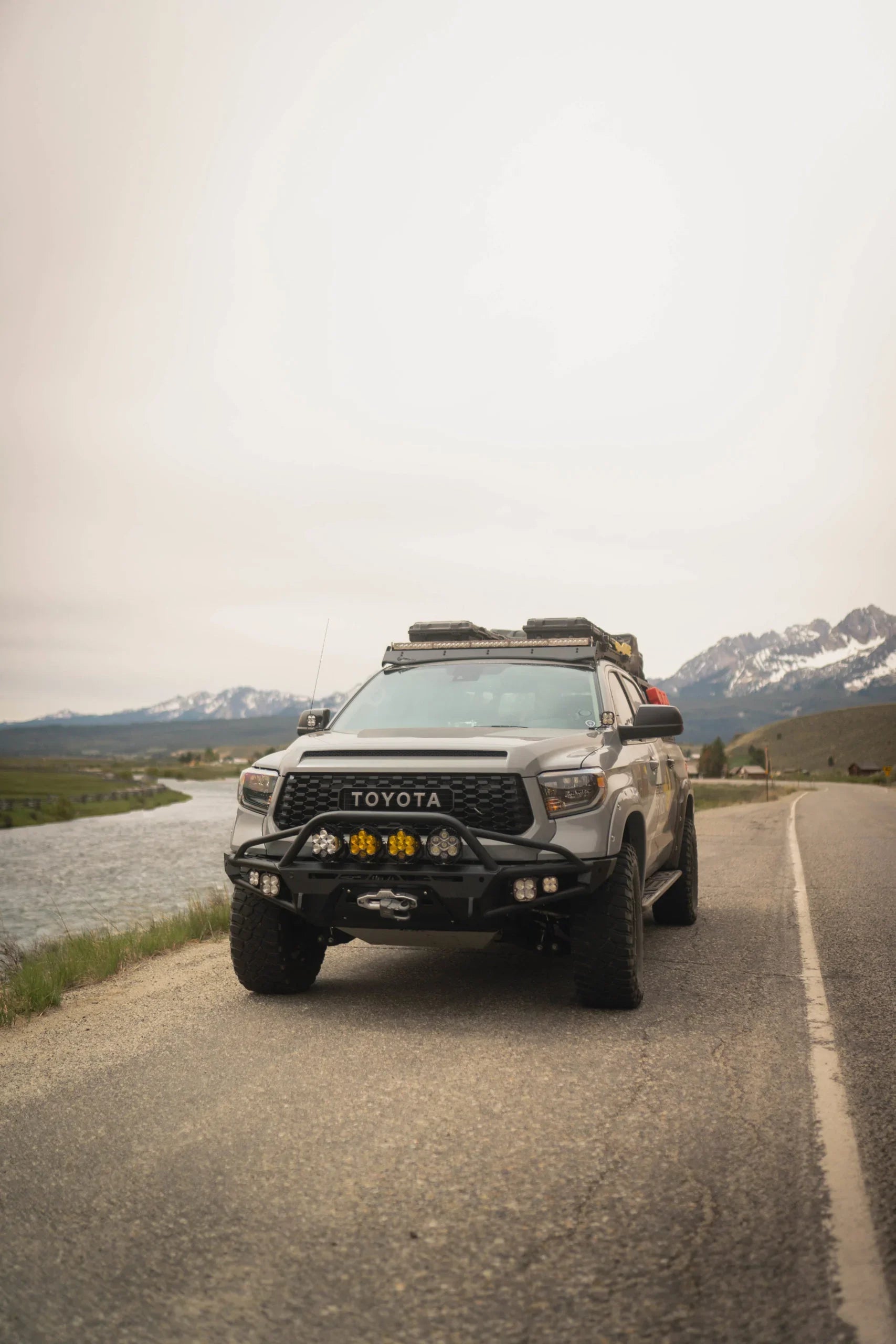 Toyota Tundra overland truck with off-road gear parked by a river, mountains in background