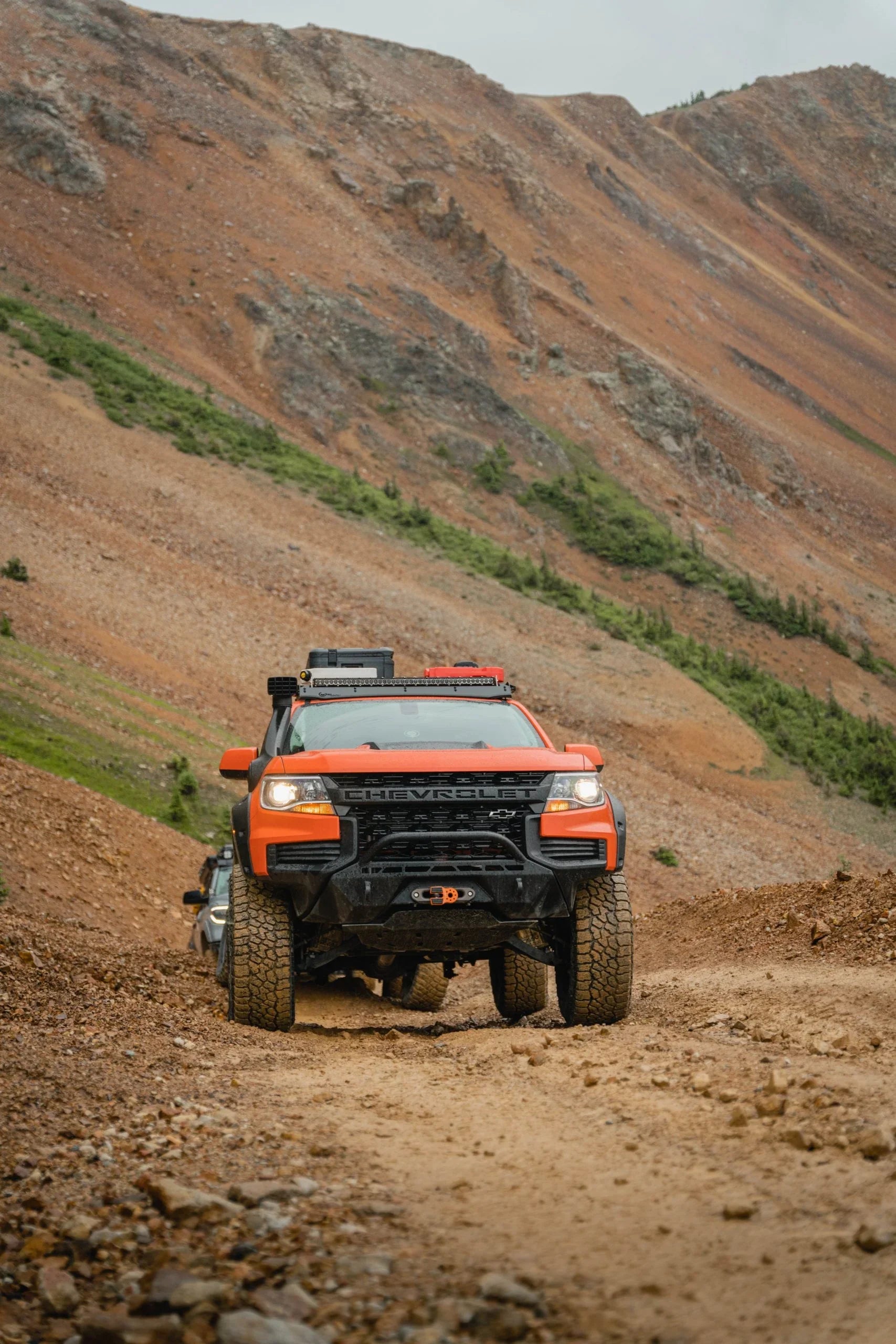 Orange Chevrolet off-road truck with gear driving rocky mountain trail, overlanding adventure