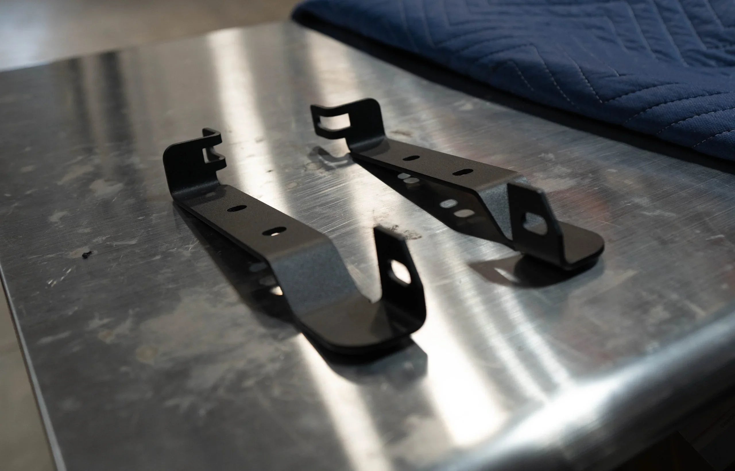 Pair of black metal mounting brackets on a stainless steel workbench for vehicle accessories