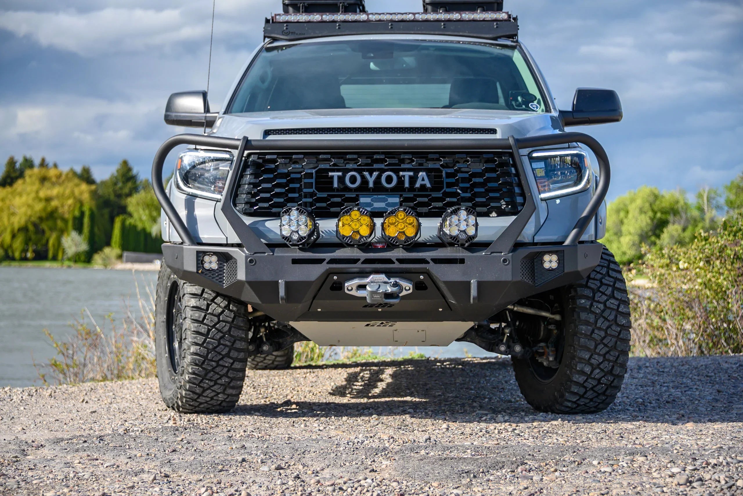 Front view of lifted Toyota Tacoma with off-road bumper, LED lights, winch, and roof rack outdoors